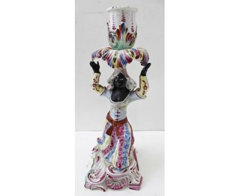 AN 18TH CENTURY PORCELAIN CANDLESTICK moulded as a Blackamoor kneeling, supporting the candle sconce aloft, upon a scrollwork