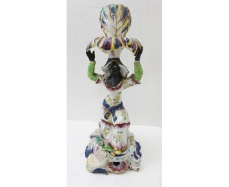 AN 18TH CENTURY PORCELAIN CANDLESTICK modelled as a Blackamoor, kneeling, supporting the candle sconce aloft, standing upon a