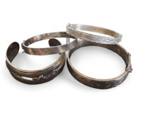 A silver hinged bangle, chased and engraved with scrolls,&nbsp;Excalibur Jewellery Ltd, Birmingham, 1974; two other silver ba