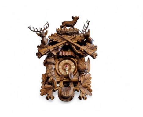 A Black Forest cuckoo clock, 9cm dial applied with Roman numerals, the case carved with dead game, deer and shot guns,&nbsp; 