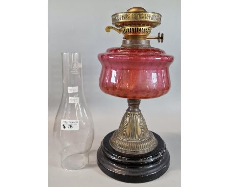 Early 20th century double oil burner lamp having Cranberry glass reservoir on brass relief and ebonised base.  (B.P. 21% + VA