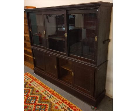 Early 20th century stained pine shop cabinet, having moulded cornice above three glazed sliding doors revealing shelf to the 