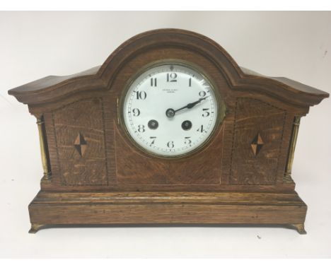 An inlaid oak mantel clock with brass pillars. French movement striking on a gong. Enamel dial maker Kendel and Dent.