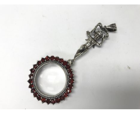 A sterling silver and garnet cherub magnifying glass pendant.