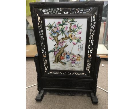A Chinese table screen with a hardwood frame enclosing a ceramic panel decorated with figures in a garden setting, approx 45c
