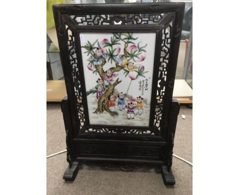 A Chinese table screen with a hardwood frame enclosing a ceramic panel decorated with figures in a garden setting, approx 45c