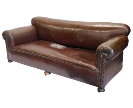 An early 20thC sofa, upholstered in brown leatherette, with a shaped back, scroll arms, embellished with brass buttons, on bu