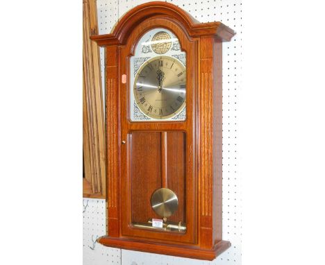 A contemporary oak drop trunk wall clock having Westminster chime, pendulum, and two weights