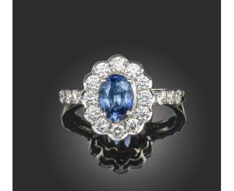 A sapphire and diamond cluster ring, the oval-cut sapphire set within a surround of round brilliant cut diamonds with further