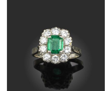 An emerald and diamond cluster ring, the step-cut emerald set within a surround of circular-cut diamonds in white gold, stamp