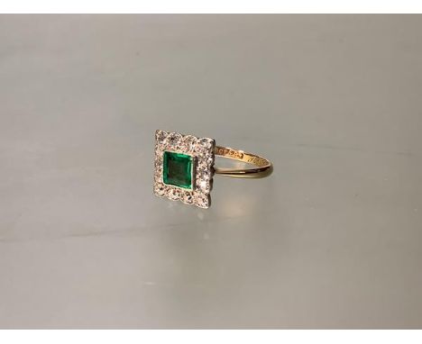 An 18ct gold and platinum, emerald and diamond cluster ring in the Art Deco taste, the collet-set square-cut emerald within a