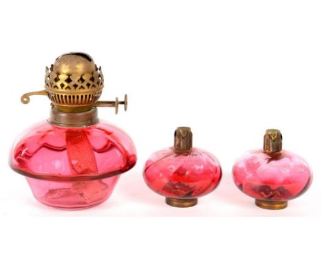 A CRANBERRY GLASS OIL LAMP FOUNT WITH BRASS BURNER AND TWO BRASS MOUNTED CRANBERRY PEG LAMPS, 19 AND 9CM H ++Good condition 