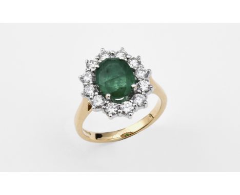 AN EMERALD AND DIAMOND CLUSTER RING the oval-shaped emerald is set within a surround of twelve circular-cut diamonds, in 18ct