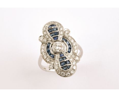 A SAPPHIRE AND DIAMOND CLUSTER RING centred with a collet set circular-cut diamond, within a surround of calibre-cut sapphire