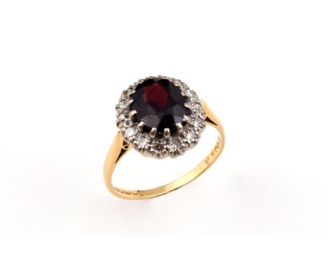 A GARNET AND DIAMOND CLUSTER RING the oval-shaped garnet is set within a surround of circular-cut diamonds in 18ct gold. Size