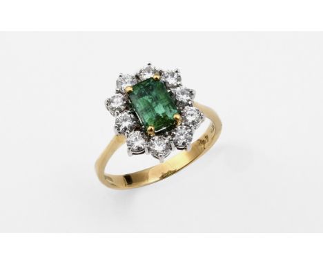 AN EMERALD AND DIAMOND CLUSTER RING the rectangular-shaped emerald is set within a surround of ten circular-cut diamonds in 1