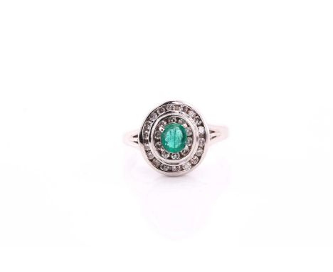 An emerald and diamond cluster ring, set with a central oval emerald measuring 5x4.5mm, surrounded by a two-tiered round bril