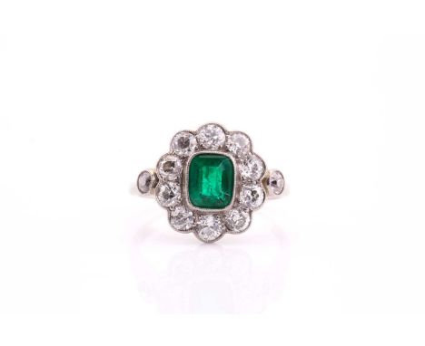 An Edwardian emerald and diamond cluster ring; the stepped rounded rectangular emerald in milegrain mount with a border of te