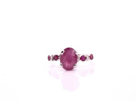 A ruby and diamond dress ring, consisting of a central oval ruby measuring 10.5x8mm claw set into a white metal collet and sh