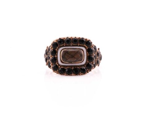 A Georgian stone set mourning ring consisting of a cased locket of hair surrounded by faceted black stones on a rose metal mo