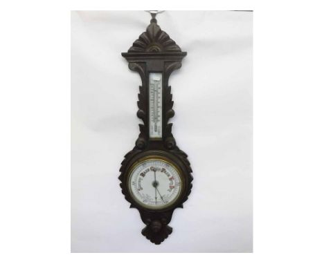 An early 20th Century Carved and Stained Oak Aneroid Wheel Barometer, the carved foliate case set with a porcelain-backed twi