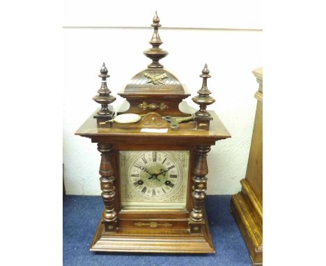 An early 20th Century Walnut and Brass Mounted Mantel Clock, the overhanging cornice surmounted by a shaped pediment with rin