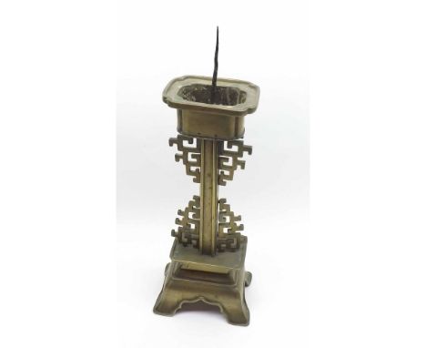 A Chinese Brass Candlestick, with shaped sconce over central column, applied with geometric mounts, terminating in a four-foo