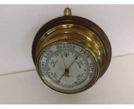 An early 20th Century Brass Cased Bulkhead Aneroid Barometer, the drum-shaped case mounted on a moulded oak mount, and set wi