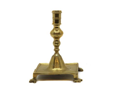 A brass candlestick,17th century, raised on a square base on 'claw' feet, 19cm highCondition ReportSome knocks and wear.