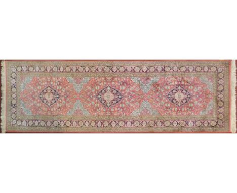 A Persian part silk runner with repeating triple medallions and scrolling floral decoration on a rouge ground within floral m