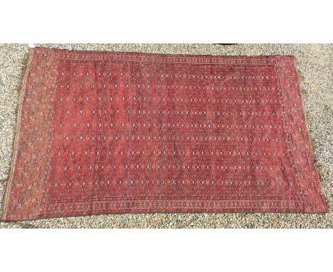 A large hand knotted Persian Bokhara carpet, the red fields with repeating geometric decoration within a triple border, 356cm