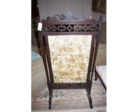 An early 20th Century stained wood fire screen, with pierced fret work and silk work picture of floral design, 124cms high.