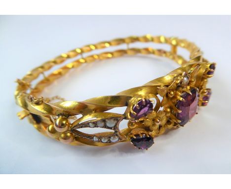 An Edwardian amethyst, half pearl and 9 carat gold hinged bangle, the top section of the openwork textured floral and scrolli
