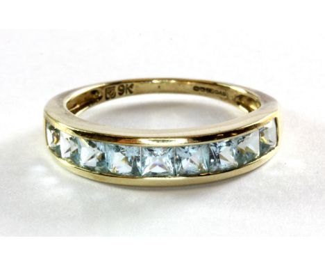 A 9ct (stamped 9k) yellow gold and blue topaz set half eternity ring, (P.5).