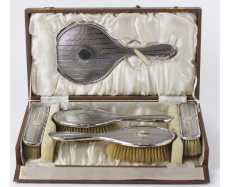 A George V silver five piece dressing table set, comprising four brushes and a hand mirror, engine turned detailing, Birmingh