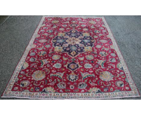 A Tabriz wool carpet, worked with a central motif and all over foliate design against a red ground, 263cm x 178cm