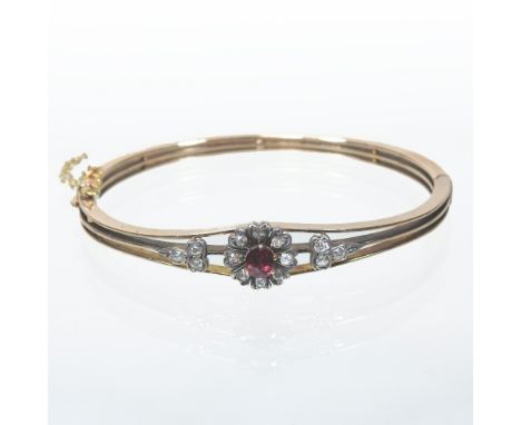 An early 20th century unmarked ladies bangle, of hinged design, set with a ruby and diamond flowerhead, flanked by diamond cl
