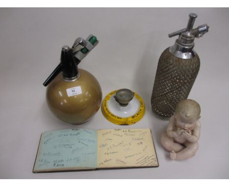 Two mid 20th Century soda siphons, an enamel advertising ashtray incorporating a dice shaker, a bisque piano doll figure and 