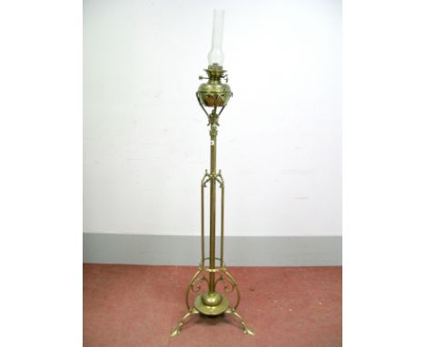 An Early XX Century Floor Standing Brass Oil Lamp, the central column with scrollwork and raised on a circular base with thre