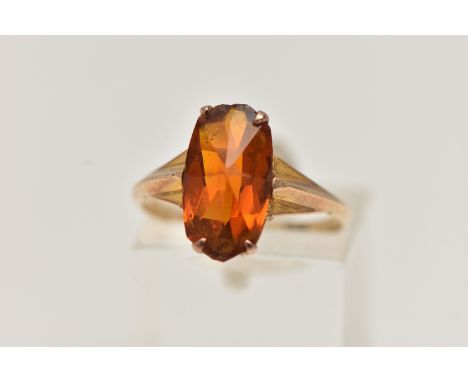 A YELLOW METAL ORANGE PASTE SET RING, fancy rectangular cut orange paste, four claw set to tapering shoulders and a polished 