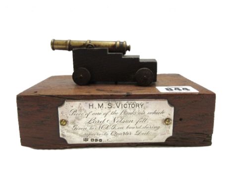 A brass and oak mounted model cannon set on timber from HMS Victory, the applied hallmarked silver plaque detailed "H.M.S Vic