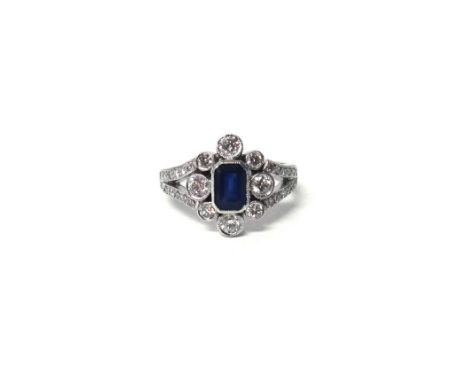A white gold, sapphire and diamond cluster ring, mounted with the cut cornered rectangular step cut sapphire at the centre, i