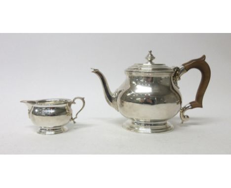 A silver teapot of oval form, the hinge lid with a turned finial, raised on an oval foot, with a wooden handle and a matching