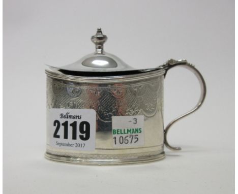 A George III silver mustard pot, of oval form, with engraved decoration and with an urn shaped finial to the hinged lid, Lond