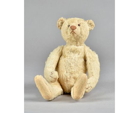 An early 20th century Steiff style teddy bear with plush golden fur, glass eyes, stitched snout, hump back and jointed limbs,