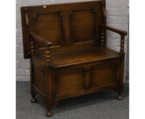 A carved oak monks bench with folding top and under seat storage. 