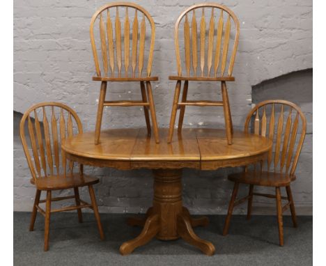 A circular light oak extending centre pedestal dining table with extra leaf, along with four slat back chairs, 150cm x 107cm 