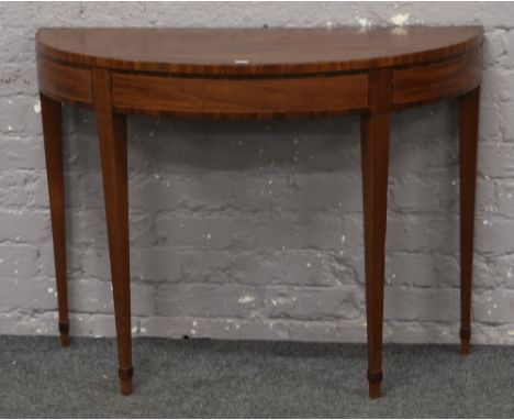 A 19th century mahogany demi lune fold over card table raised on tapering supports and with strung inlay. 