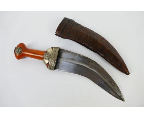 An Arab jambiya with 19 cm (l) blade having medial ridge, amber coloured white metal mounted grip, contained in sheath. [W]
N