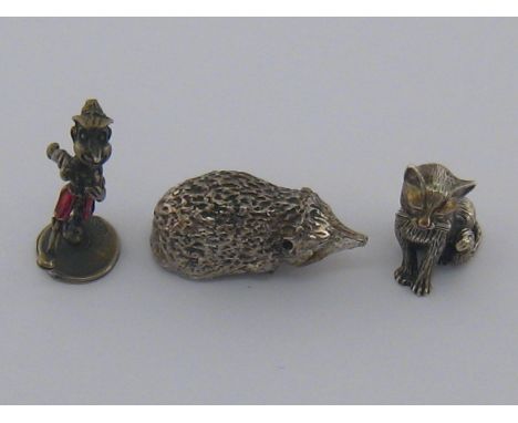 A silver Pinocchio figure with red enamel shorts, marked 800, together with a white metal hedgehog and a white metal sitting 